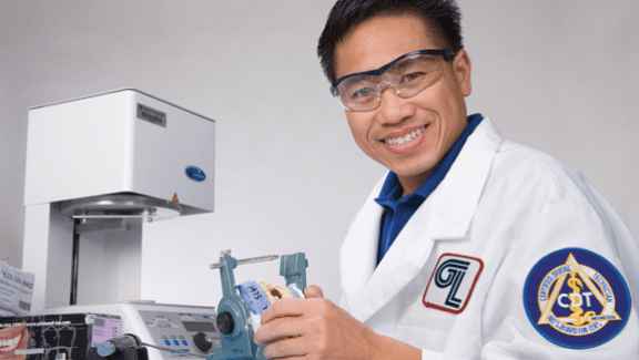 Male scientist wearing Glidewell Dental lab coat in from of dental manufacturing machines