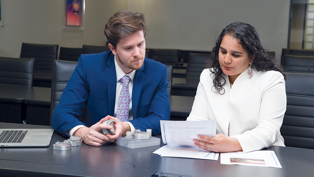 Man, Brett Allen, peering over document held by Clinical Research Manager, Dr. Mayuri Kerr
