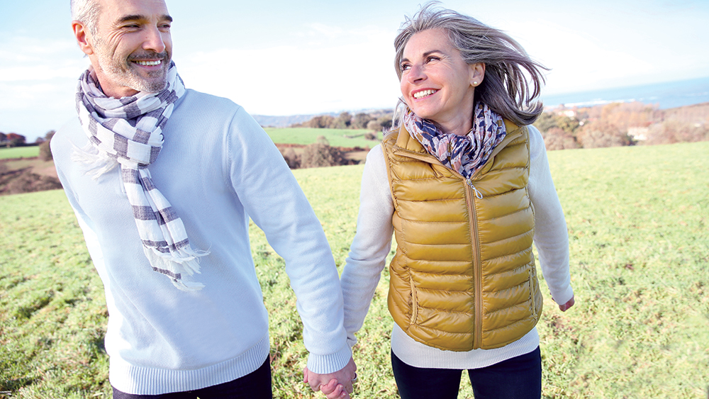Older aged-couple running through grassy field holding hands